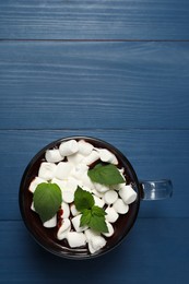 Photo of Glass cup of delicious hot chocolate with marshmallows and fresh mint on blue wooden table, top view. Space for text