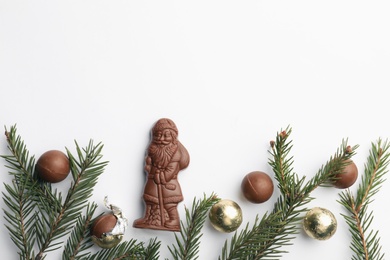 Flat lay composition with chocolate Santa Claus, fir tree twigs and sweets on white background, space for text