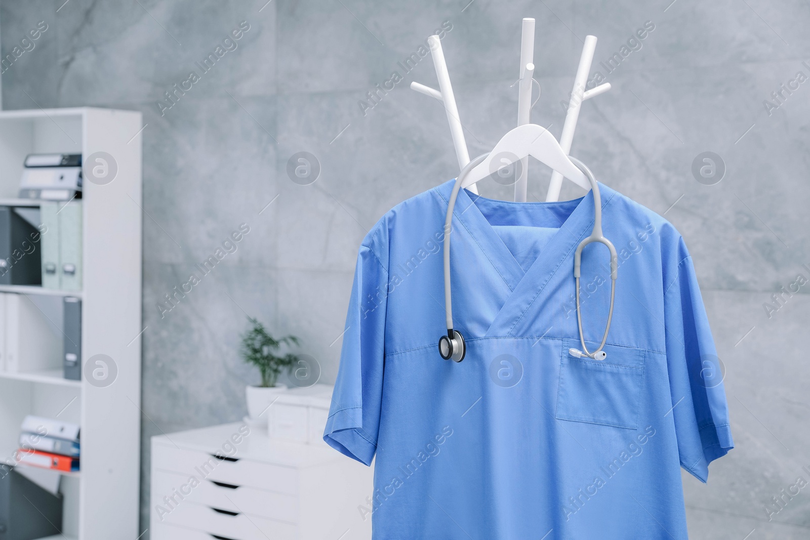 Photo of Blue medical uniform and stethoscope hanging on rack in clinic. Space for text