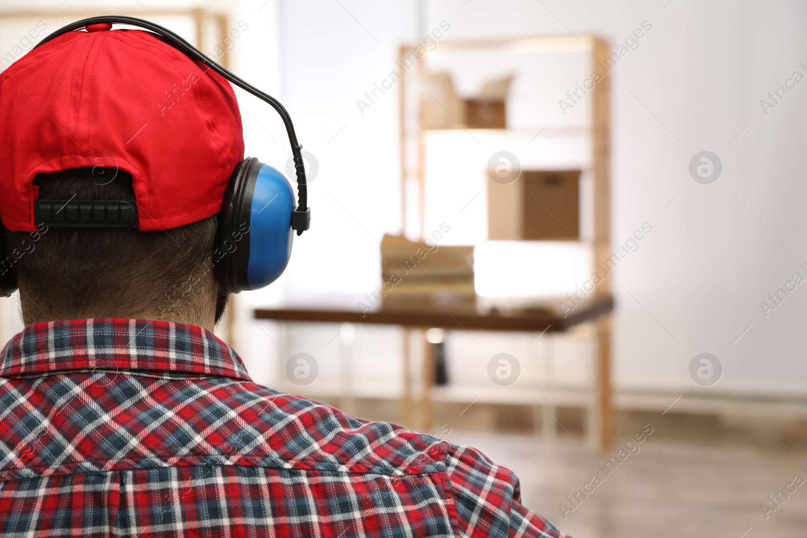 Photo of Worker wearing safety headphones indoors, back view. Hearing protection device