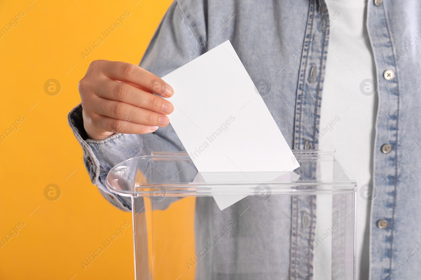 Photo of Woman putting her vote into ballot box on orange background, closeup