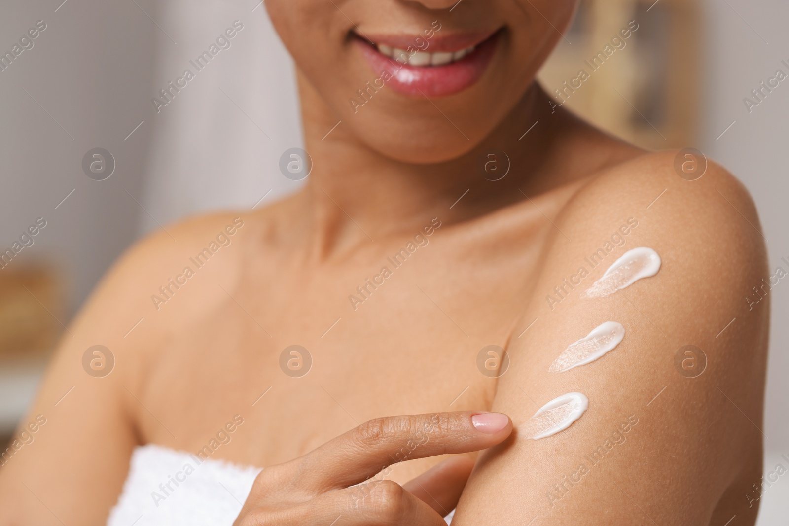 Photo of Beautiful young woman applying body cream onto arm on blurred background, closeup