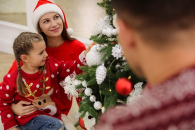 Happy family with cute child decorating Christmas tree together indoors