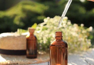 Photo of Woman dripping chamomile essential oil into bottle at white table, closeup. Space for text