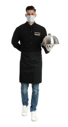 Photo of Waiter in medical face mask holding tray with lid on white background