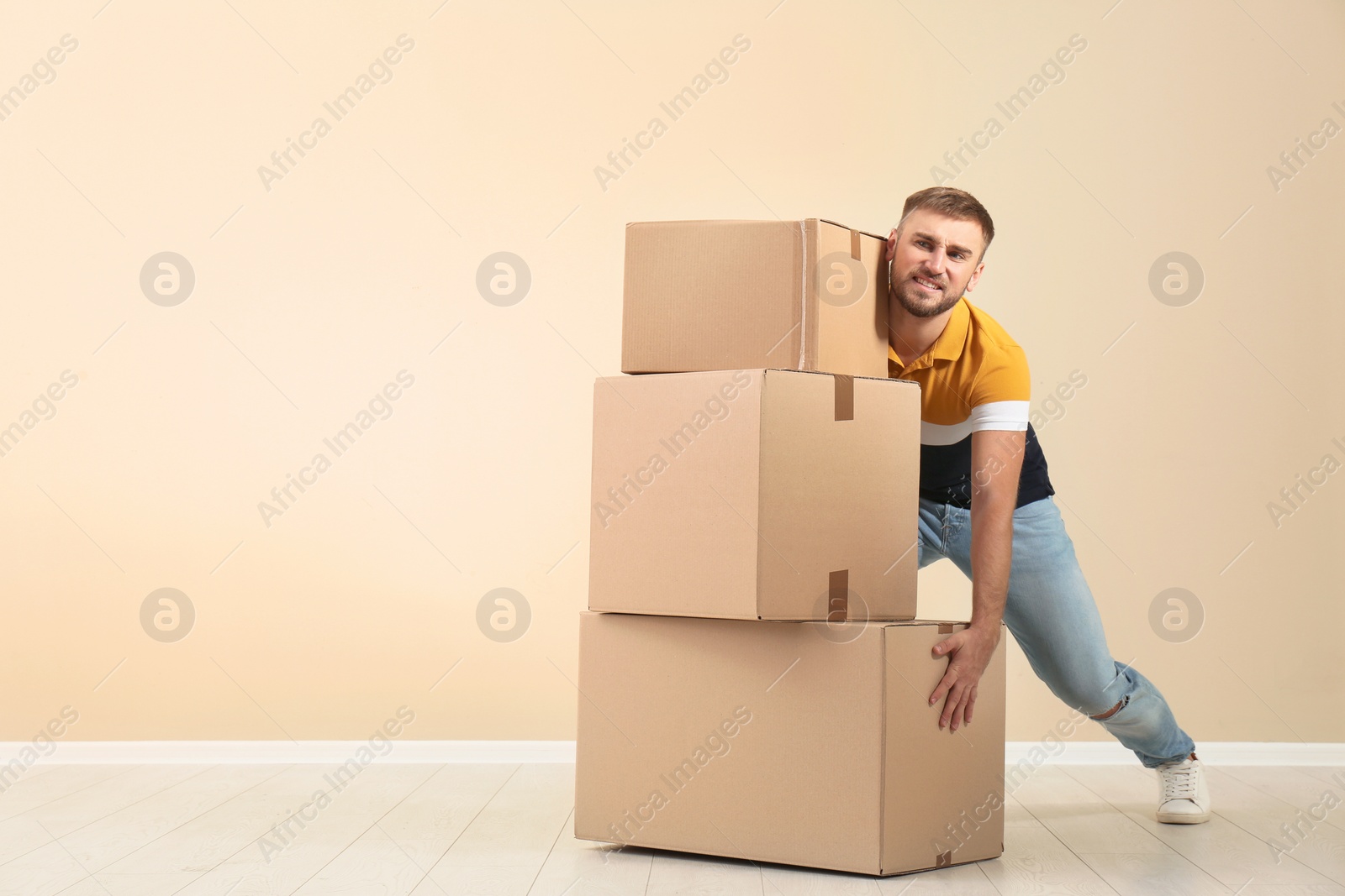 Photo of Full length portrait of young man lifting carton boxes near color wall. Posture concept