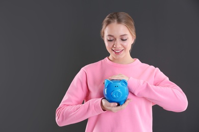 Happy young woman with piggy bank and space for text on grey background. Money saving