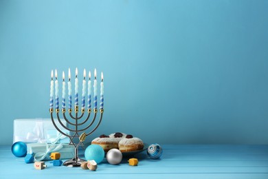 Composition with Hanukkah menorah, dreidels, donuts and gift boxes on table against light blue background. Space for text