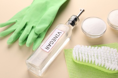 Photo of Eco friendly natural cleaners. Vinegar in bottle, bowls of soda, brush and gloves on beige background