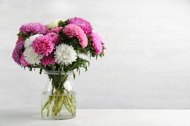 Beautiful asters in vase on table against white background, space for text. Autumn flowers