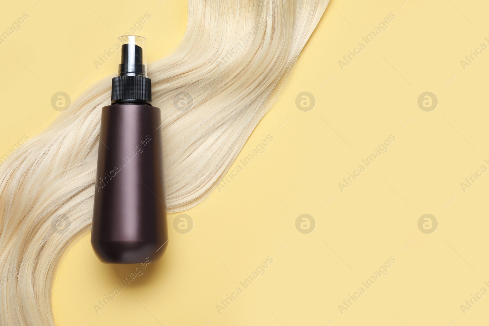 Photo of Spray bottle with thermal protection and lock of blonde hair on yellow background, flat lay. Space for text