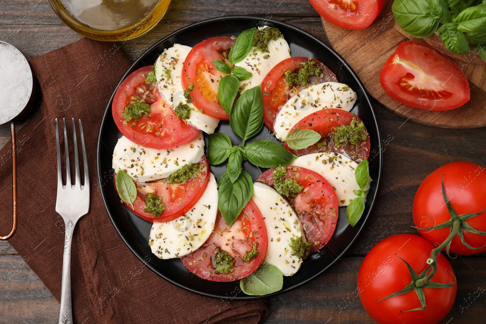Photo of Plate of delicious Caprese salad with pesto sauce and ingredients on wooden table, flat lay