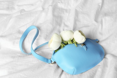 Photo of Stylish bump bag with spring flowers on crumpled white sheet