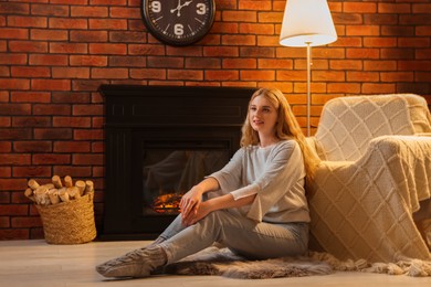 Beautiful young woman resting near fireplace at home