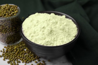 Photo of Mung bean flour in bowl and seeds on white marble table, closeup