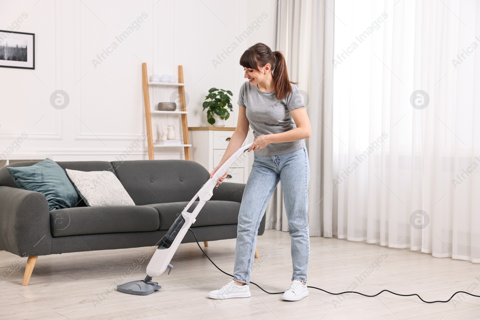 Photo of Happy young housewife cleaning floor with steam mop at home