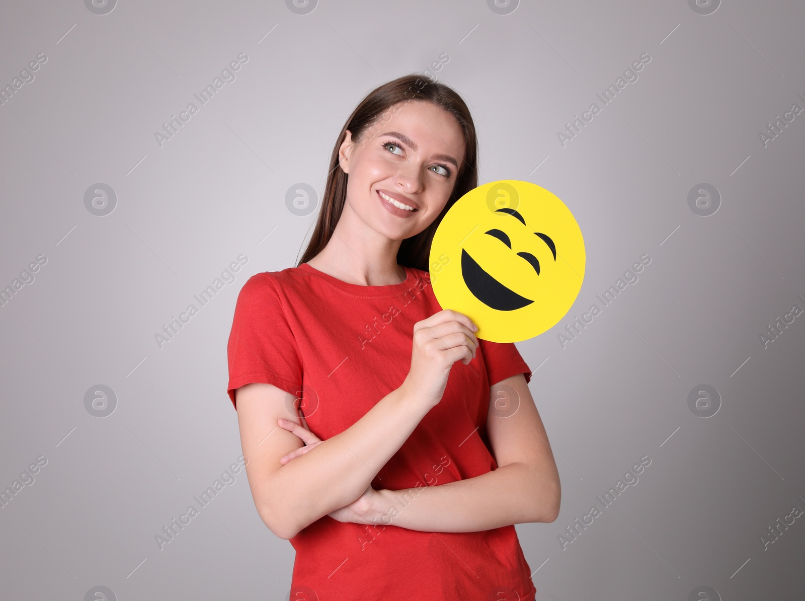 Photo of Happy young woman with laughing emoji on grey background