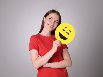 Photo of Happy young woman with laughing emoji on grey background