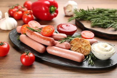 Photo of Delicious vegetarian sausages with rosemary, vegetables and sauces on wooden table
