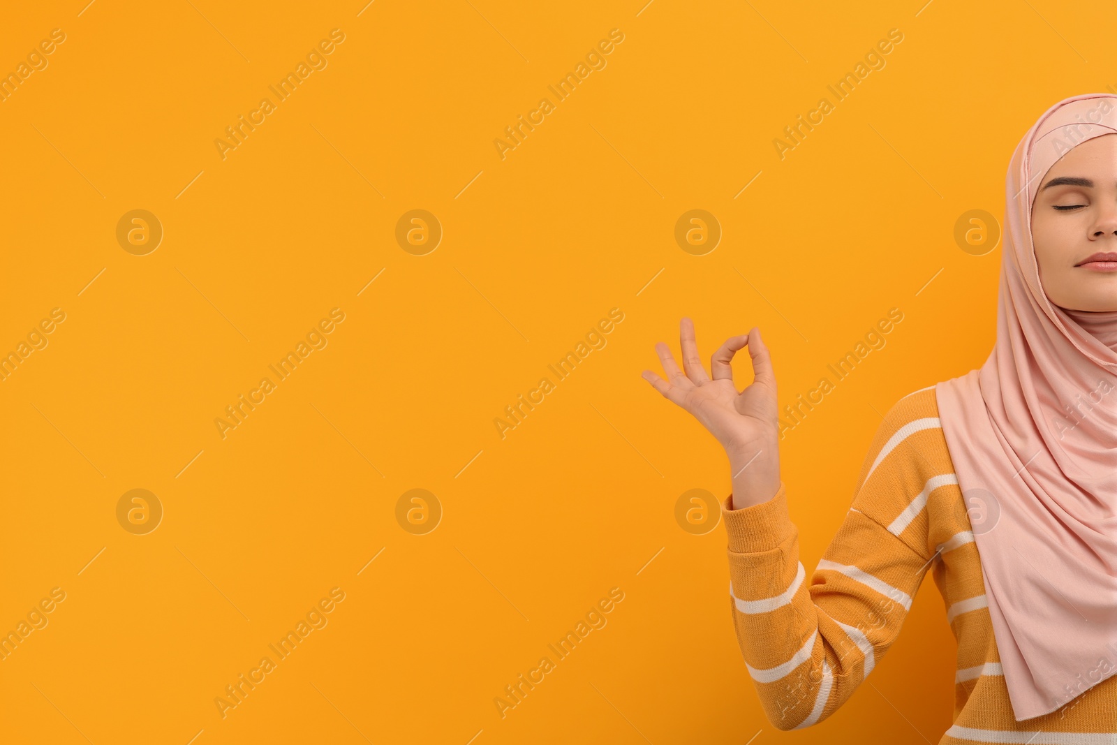 Photo of Muslim woman in hijab meditating on orange background, space for text