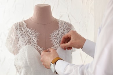 Dressmaker working with wedding dress on mannequin in atelier, closeup