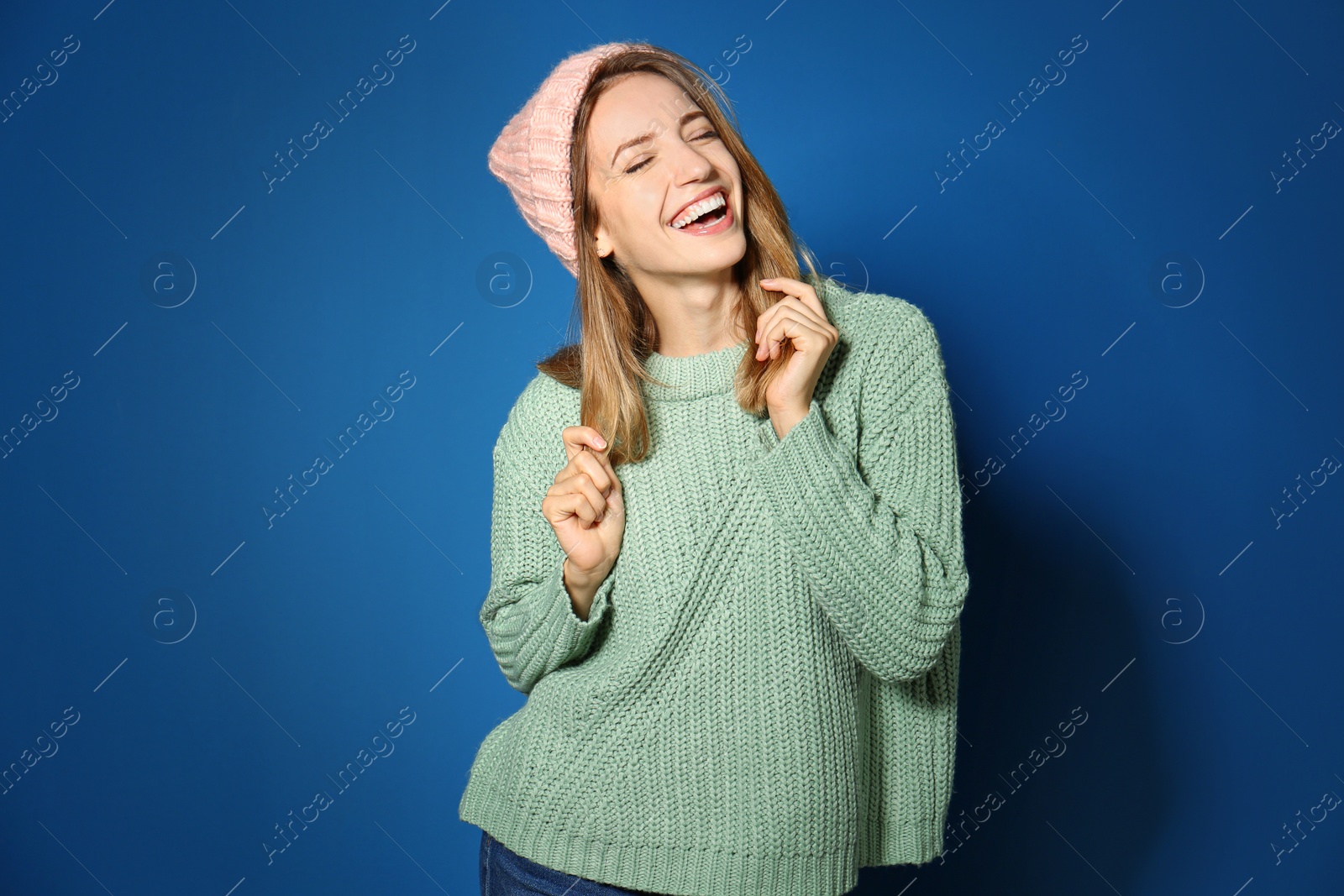 Image of Happy young woman wearing warm sweater and knitted hat on blue background