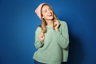 Image of Happy young woman wearing warm sweater and knitted hat on blue background