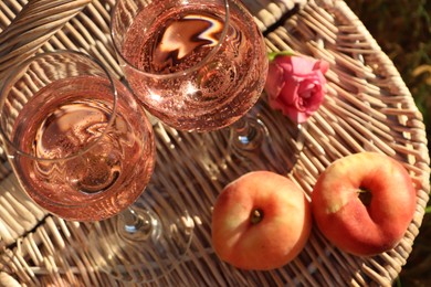 Photo of Glassesdelicious rose wine, flower and peaches on wicker basket outside, above view. Space for text