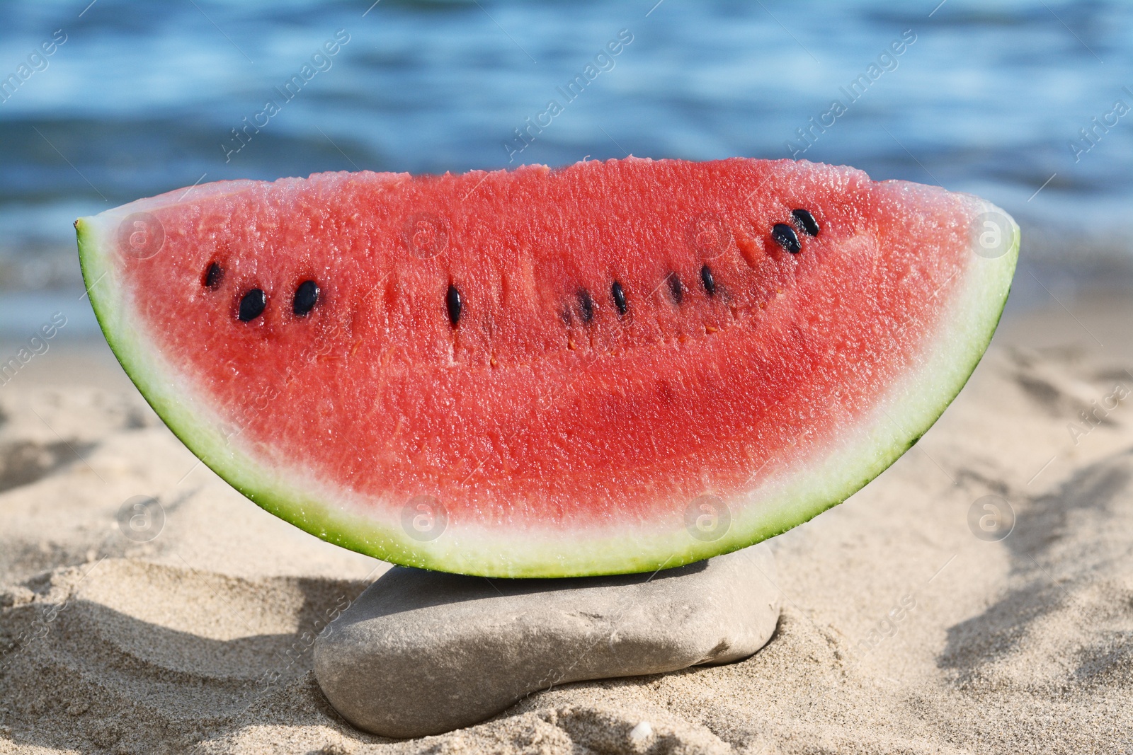 Photo of Slice of fresh juicy watermelon near sea, closeup