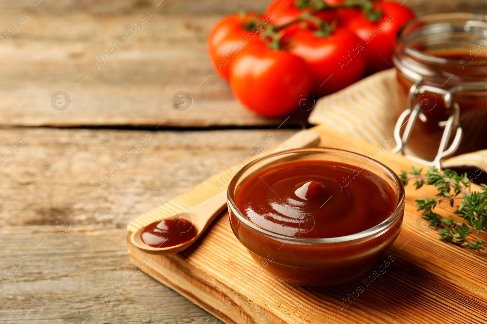 Photo of Tasty barbeque sauce in bowl and spoon on wooden table, closeup. Space for text