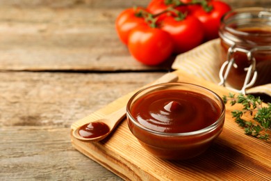 Photo of Tasty barbeque sauce in bowl and spoon on wooden table, closeup. Space for text
