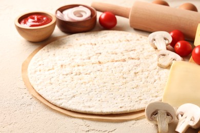 Photo of Pizza base, ketchup and products on light textured table, closeup