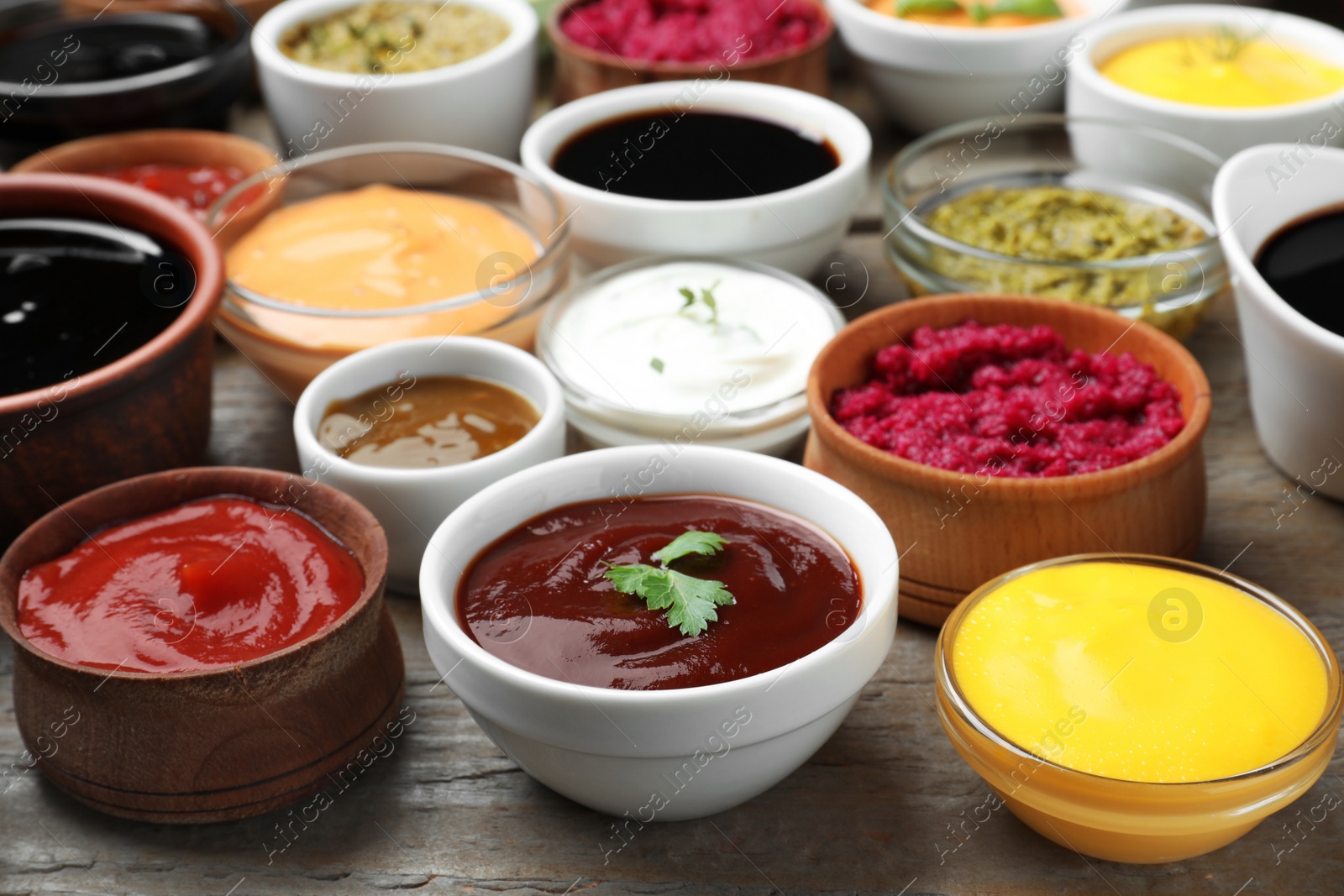 Photo of Many bowls with different sauces and herbs on wooden table