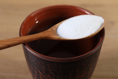 Photo of Glass of water and spoon with baking soda on table, closeup