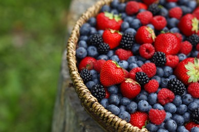 Wicker bowl with different fresh ripe berries outdoors, closeup. Space for text