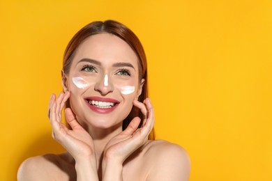 Beautiful young woman with sun protection cream on her face against orange background, space for text