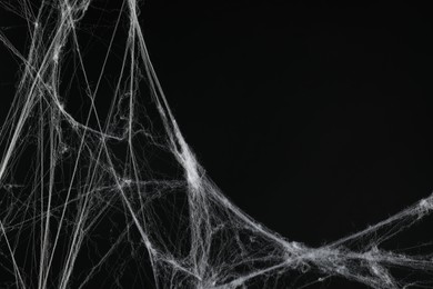 Photo of Creepy white cobweb on black background, closeup. Space for text