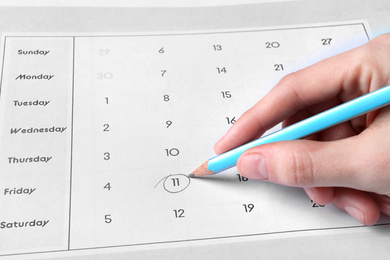 Woman marking date in calendar with pencil, closeup