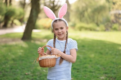 Easter celebration. Cute little girl in bunny ears holding wicker basket outdoors