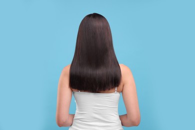 Woman with healthy hair on light blue background, back view