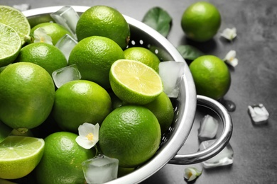 Photo of Colander with fresh ripe limes and ice cubes on table, closeup