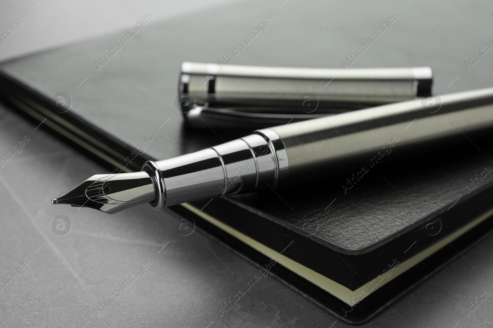 Photo of Stylish fountain pen, cap and leather notebook on light grey textured table, closeup