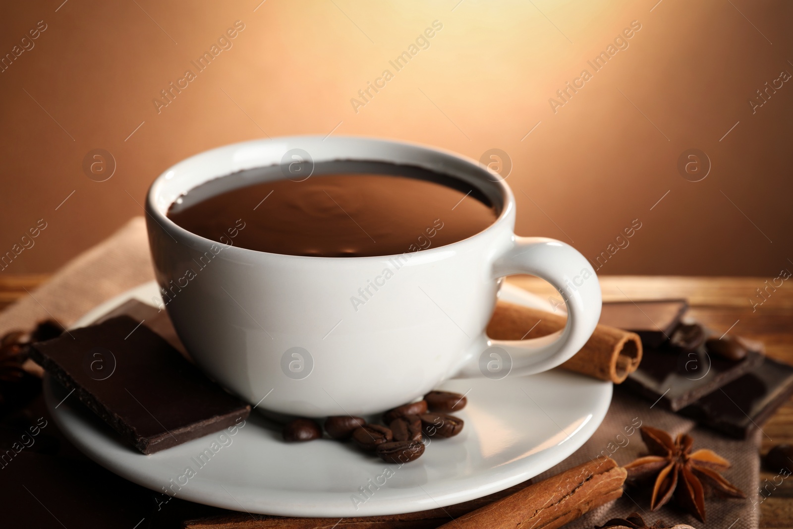 Photo of Cup of delicious hot chocolate, spices and coffee beans on wooden table