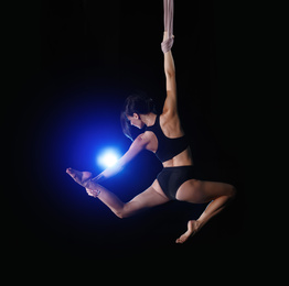 Young woman performing acrobatic element on aerial silk indoors