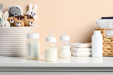 Photo of Feeding bottles with milk and other baby accessories on white table near beige wall