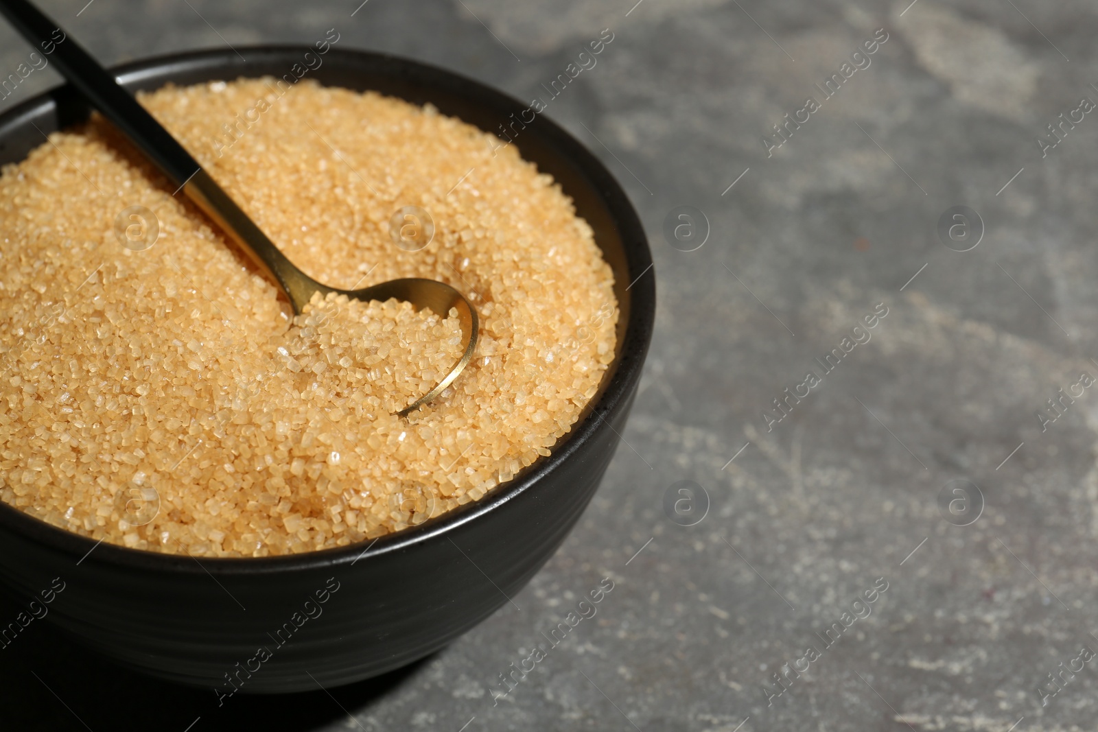 Photo of Brown sugar in bowl and spoon on grey textured table, closeup. Space for text