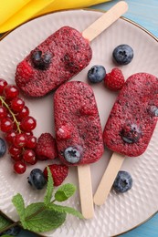 Photo of Plate of tasty berry ice pops on blue table, top view. Fruit popsicle