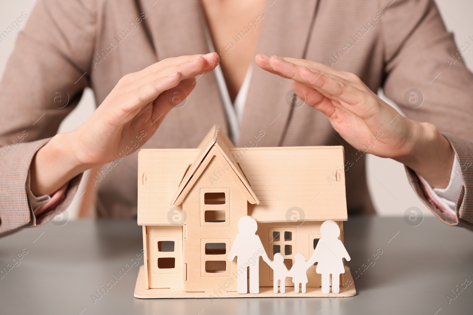 Photo of Female agent covering house model and family at table, closeup. Home insurance