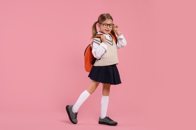 Happy schoolgirl in glasses with backpack on pink background