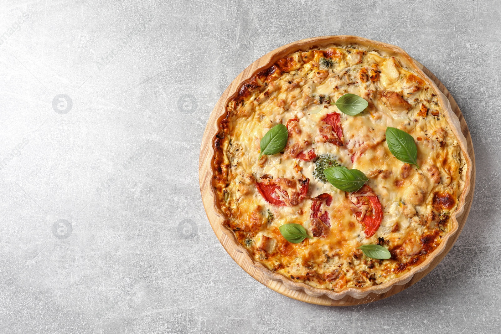 Photo of Tasty quiche with tomatoes, basil and cheese on light table, top view. Space for text